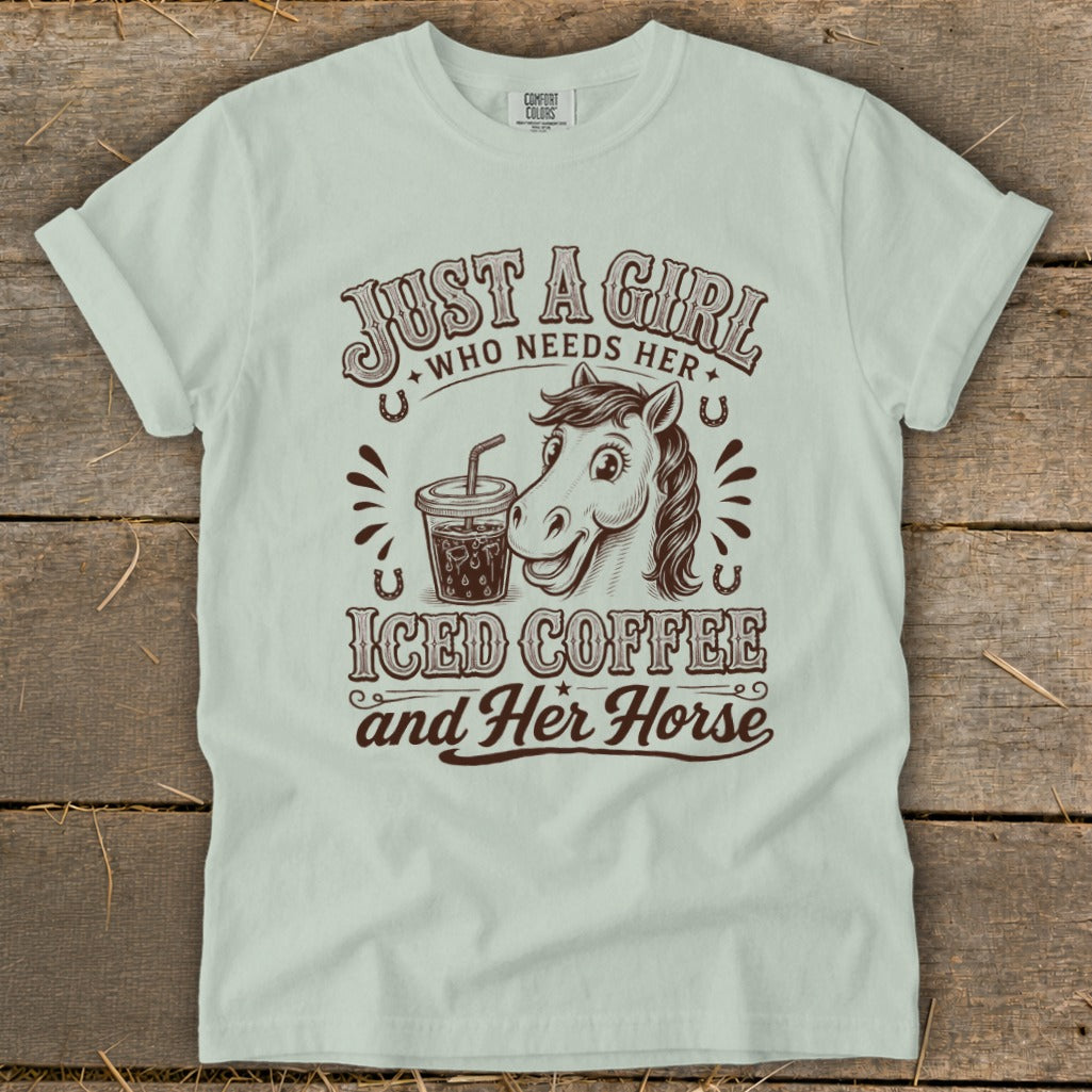 Light green t-shirt featuring brown text reading "Just A Girl Who Needs Her Iced Coffee and Her Horse" alongside an illustrated horse and iced coffee.