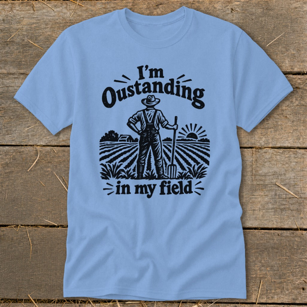 Light blue t-shirt with black graphic of farmer in field saying "I'm Oustanding in my field."