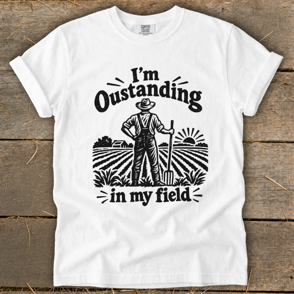 White t-shirt with graphic of farmer in field reading "I'm Oustanding in my field".