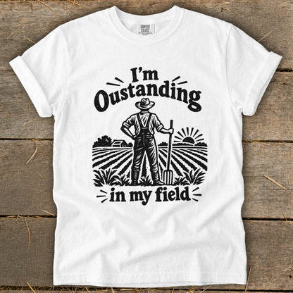 White t-shirt with graphic of farmer in field reading "I'm Oustanding in my field".