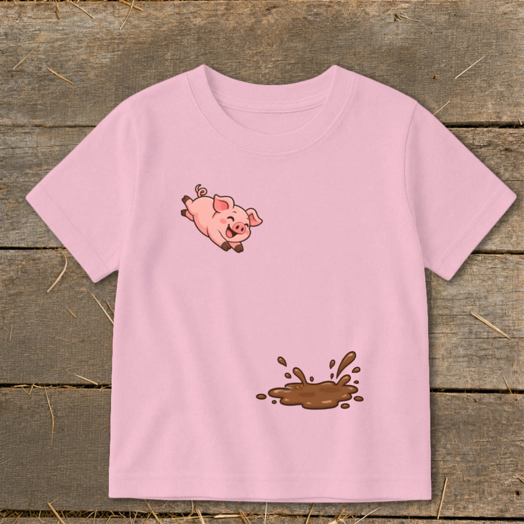 Pink t-shirt with a cartoon pig jumping over a mud puddle graphic.