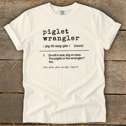 Cream t-shirt with black text defining "piglet wrangler" and "pen escape expert."