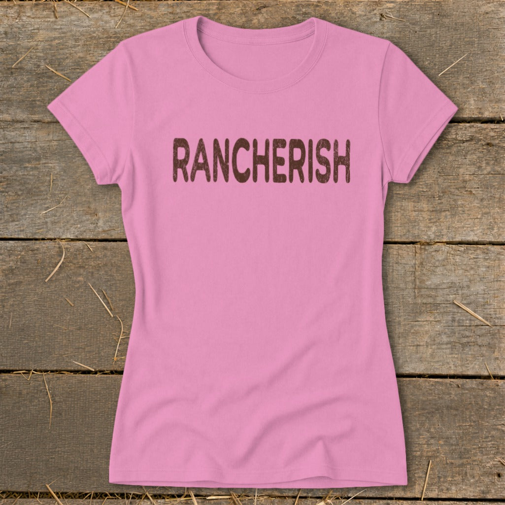 Pink t-shirt with brown distressed "RANCHERISH" text on a wooden background.