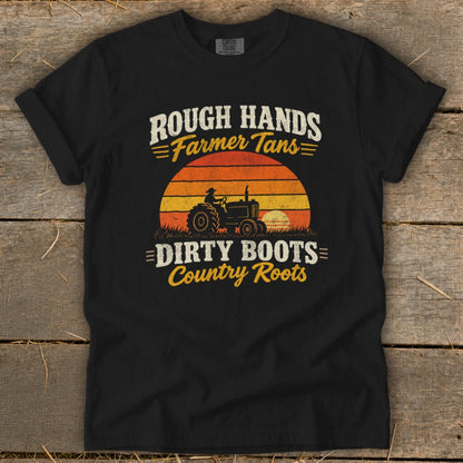 A black t-shirt featuring distressed white and yellow text that reads "Rough Hands Farmer Tans Dirty Boots Country Roots" surrounding a retro tractor and sunset graphic.