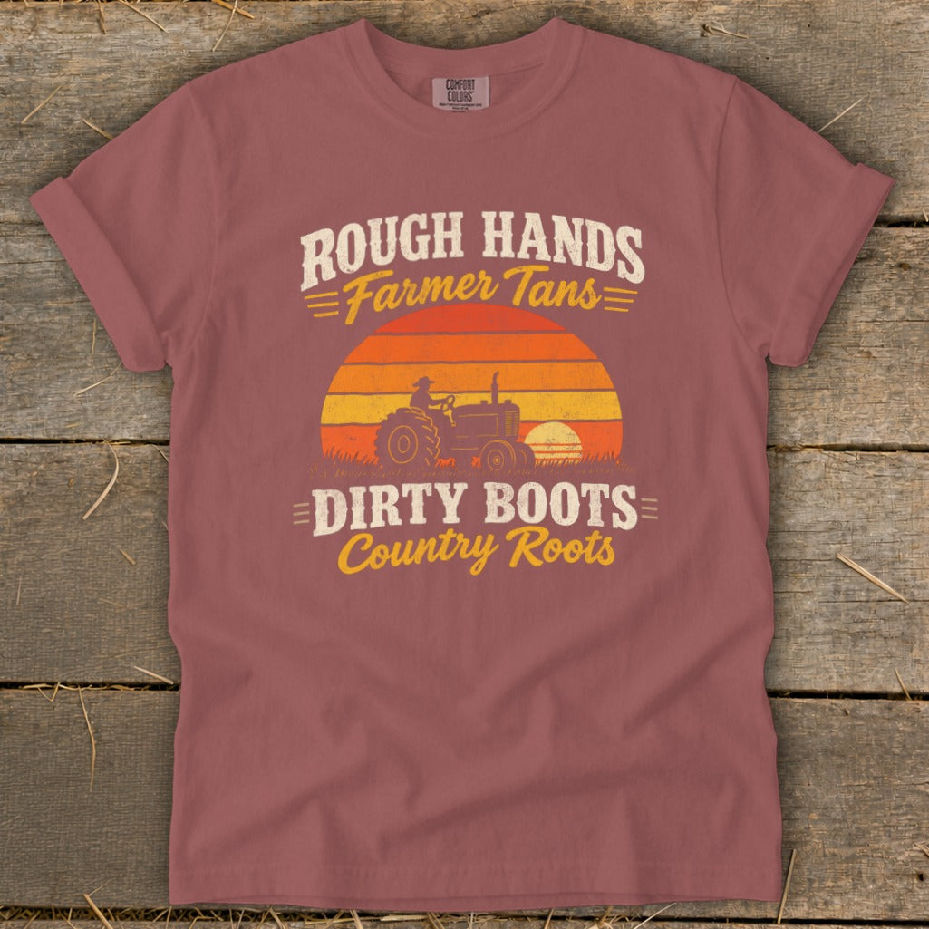 A mauve t-shirt with a vintage graphic of a tractor against a sunset and text reading Rough Hands Farmer Tans Dirty Boots Country Roots.
