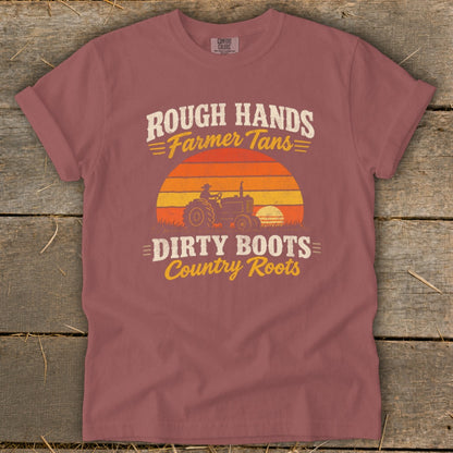 A mauve t-shirt with a vintage graphic of a tractor against a sunset and text reading Rough Hands Farmer Tans Dirty Boots Country Roots.