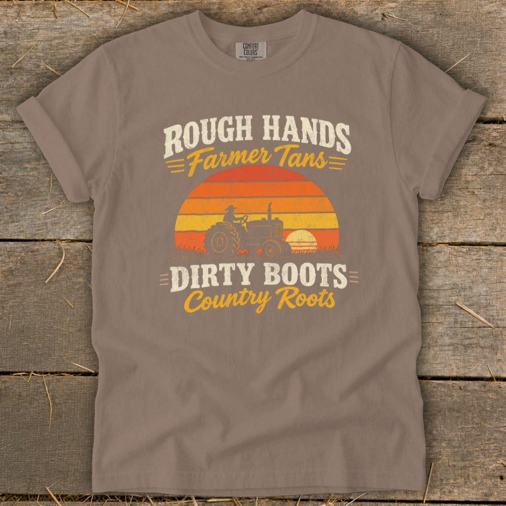 A gray t-shirt featuring a retro graphic of a tractor, sunset, and text reading Rough Hands Farmer Tans Dirty Boots Country Roots.
