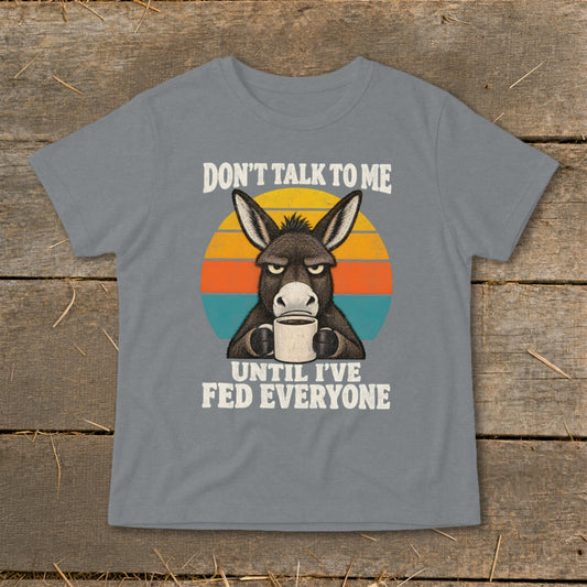 A grey t-shirt featuring a grumpy donkey drinking coffee against a retro sunset graphic with text.