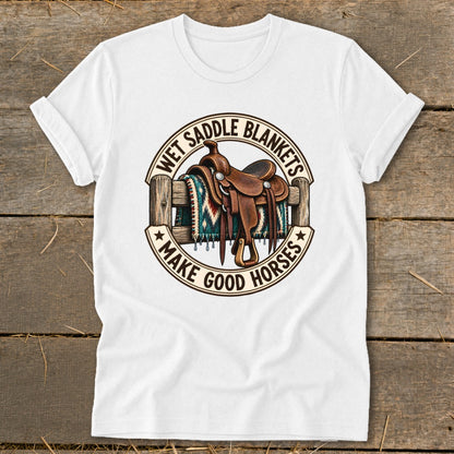 White t-shirt with a saddle and blanket on a fence, text reads "WET SADDLE BLANKETS MAKE GOOD HORSES".