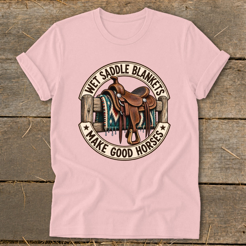 Pink t-shirt graphic with saddle on fence and text "WET SADDLE BLANKETS MAKE GOOD HORSES".