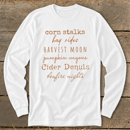 White long-sleeve shirt with "corn stalks," "hay rides," "Harvest Moon," "pumpkin wagons," "Cider Donuts," and "bonfire nights" text.