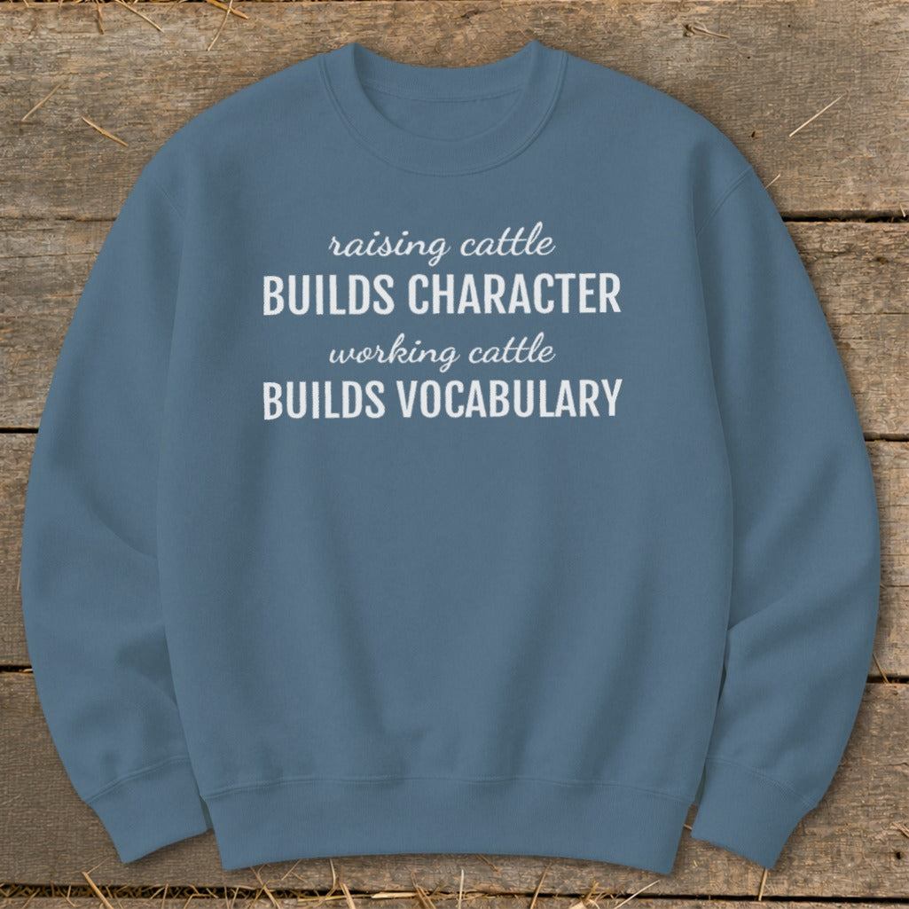 Blue sweatshirt with white text: "raising cattle BUILDS CHARACTER, working cattle BUILDS VOCABULARY."