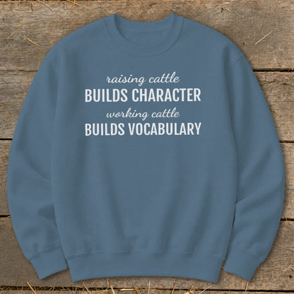 Blue sweatshirt with white text: "raising cattle BUILDS CHARACTER, working cattle BUILDS VOCABULARY."