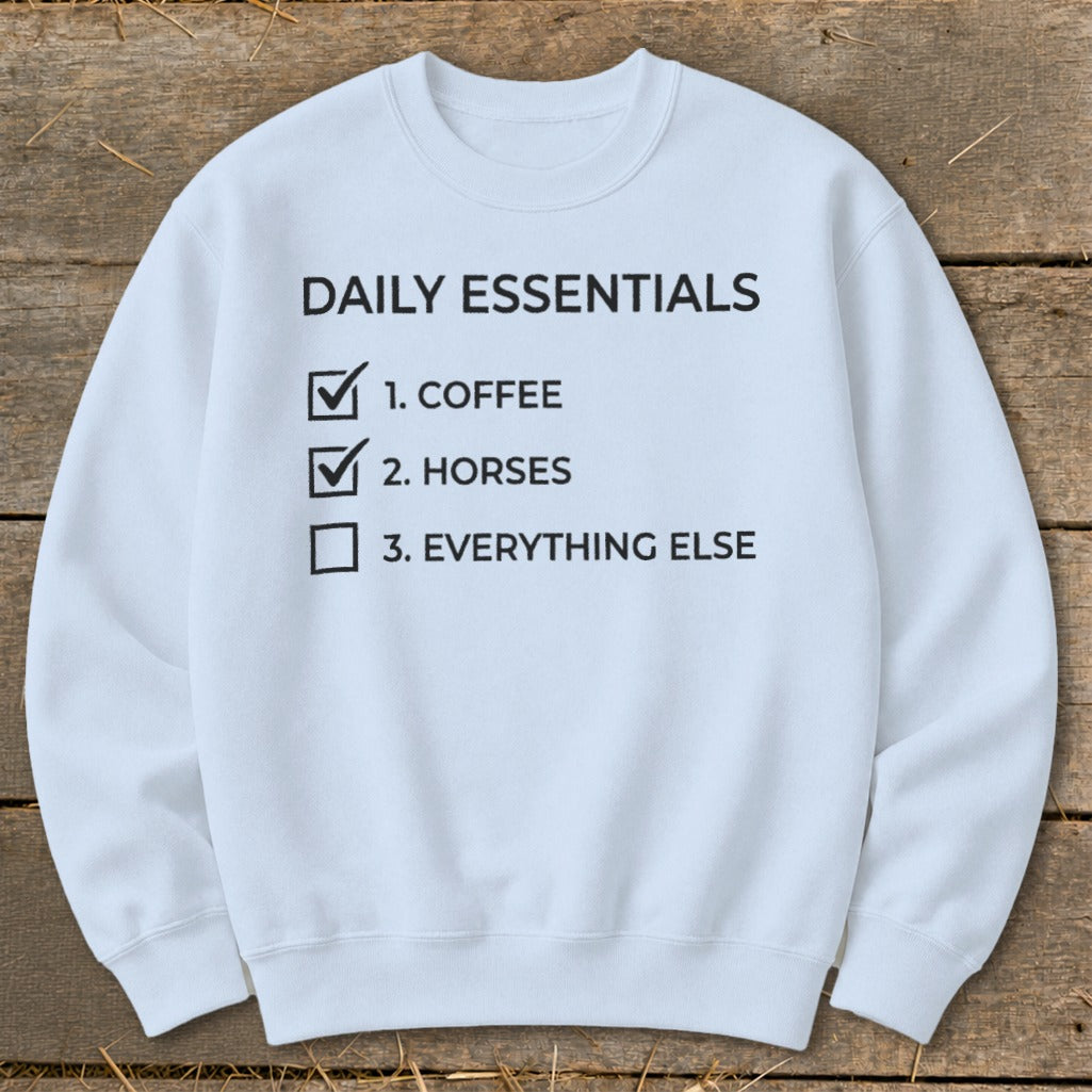 Light blue sweatshirt with black text listing "Daily Essentials": coffee, horses, and everything else.