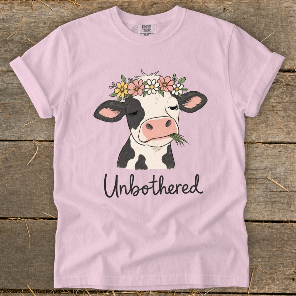 Pink t-shirt with a cow wearing a flower crown and eating grass, text reads "Unbothered".