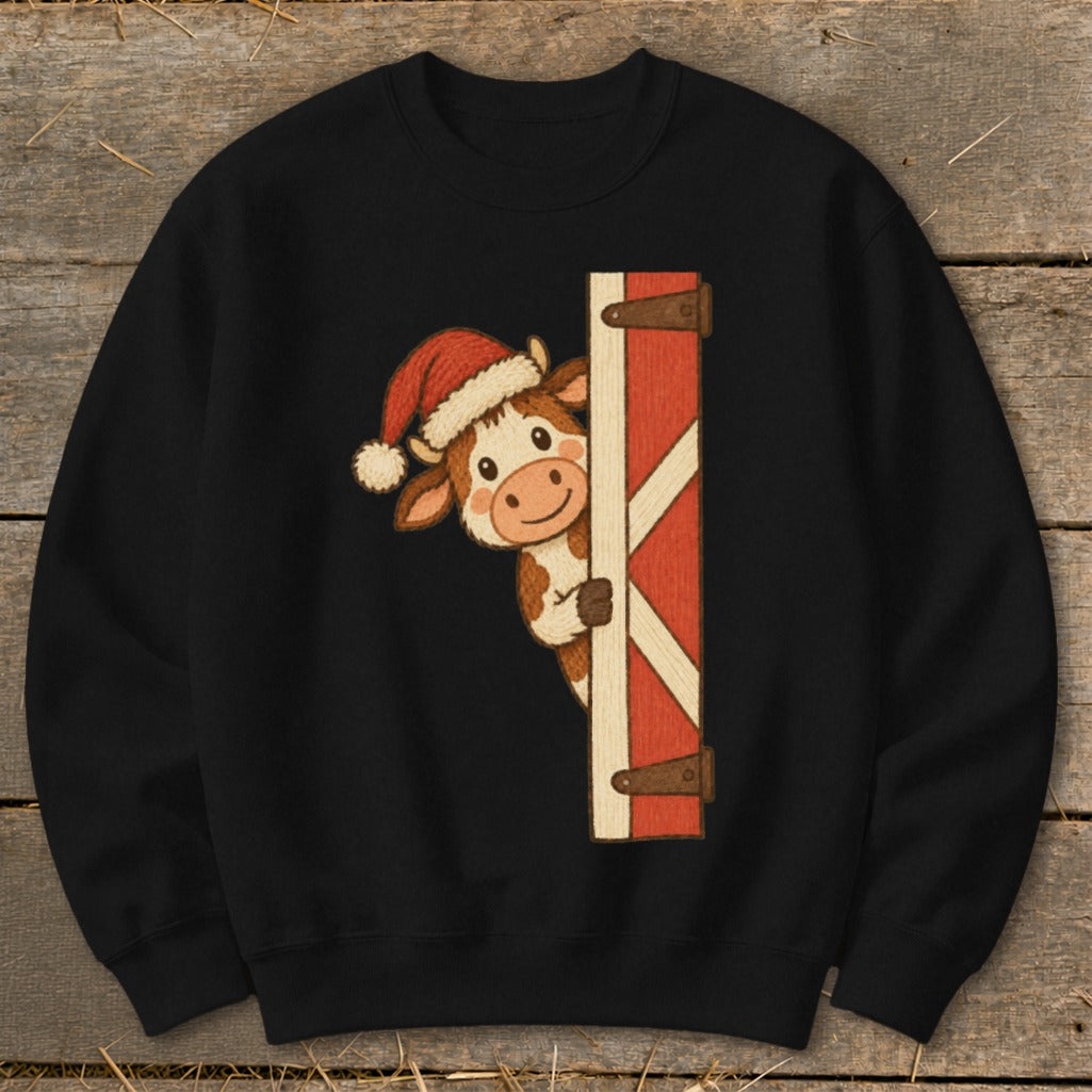 Black sweatshirt featuring a cow wearing a Santa hat peeking from behind a red barn door.