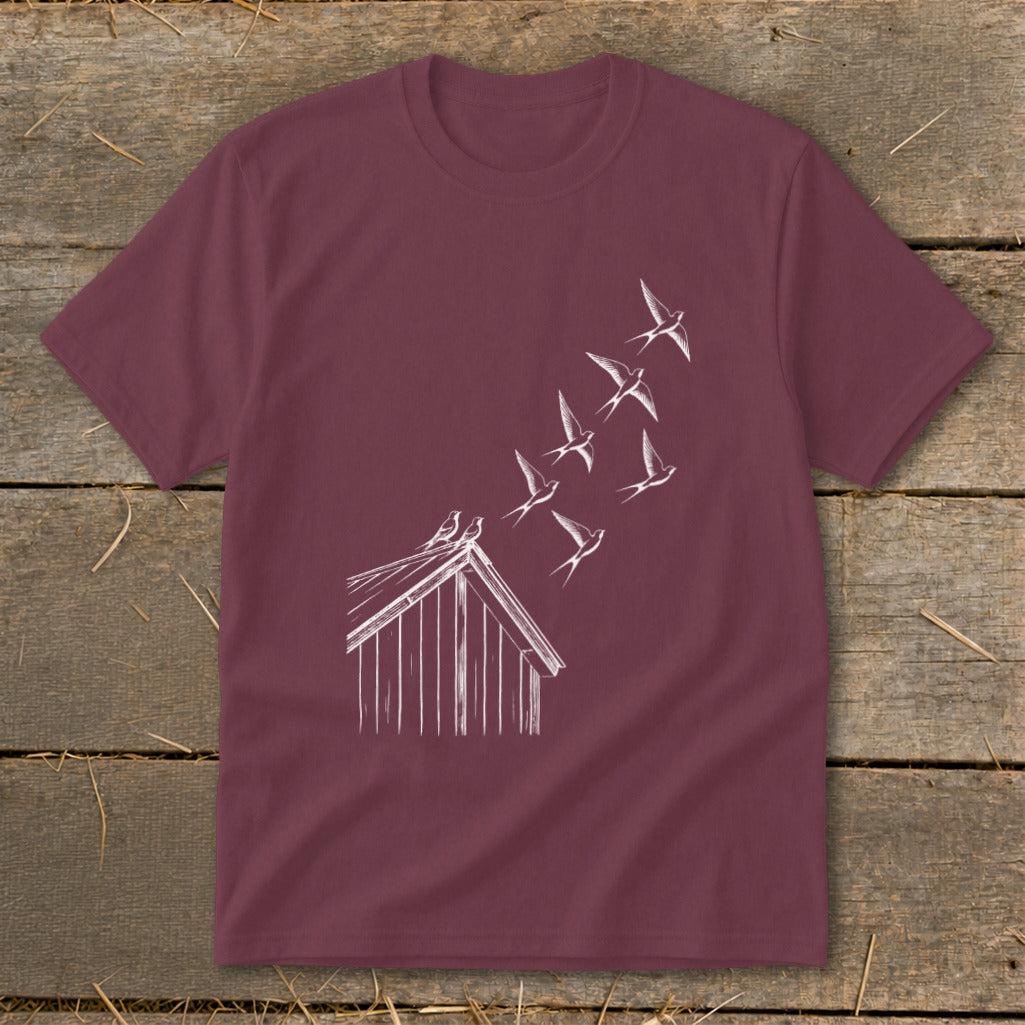 A maroon short-sleeve t-shirt with a white line drawing of birds flying from a barn roof.