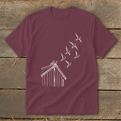 A maroon short-sleeve t-shirt with a white line drawing of birds flying from a barn roof.