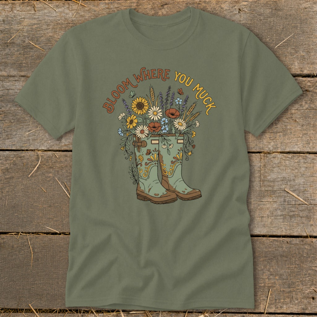 Green t-shirt with graphic of gardening boots filled with flowers and text "Bloom Where You Muck".