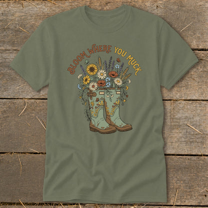 Green t-shirt with graphic of gardening boots filled with flowers and text "Bloom Where You Muck".