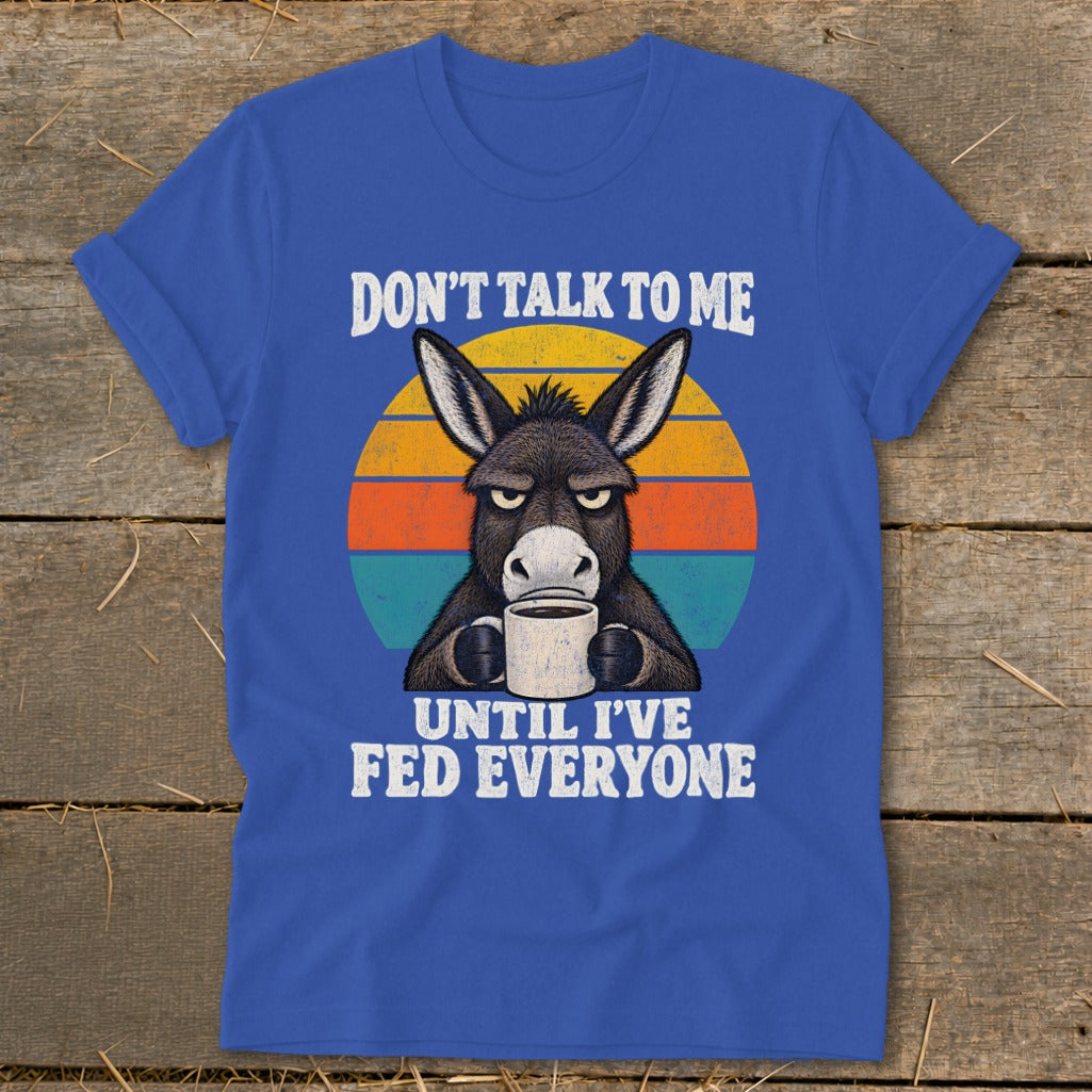 Blue t-shirt featuring a grumpy donkey holding a coffee mug with the text DON'T TALK TO ME UNTIL I'VE FED EVERYONE.