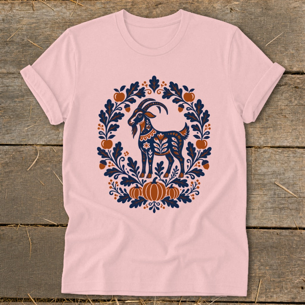 Light pink crewneck t-shirt featuring a folk-art style illustration of a goat surrounded by pumpkins, leaves, and acorns.