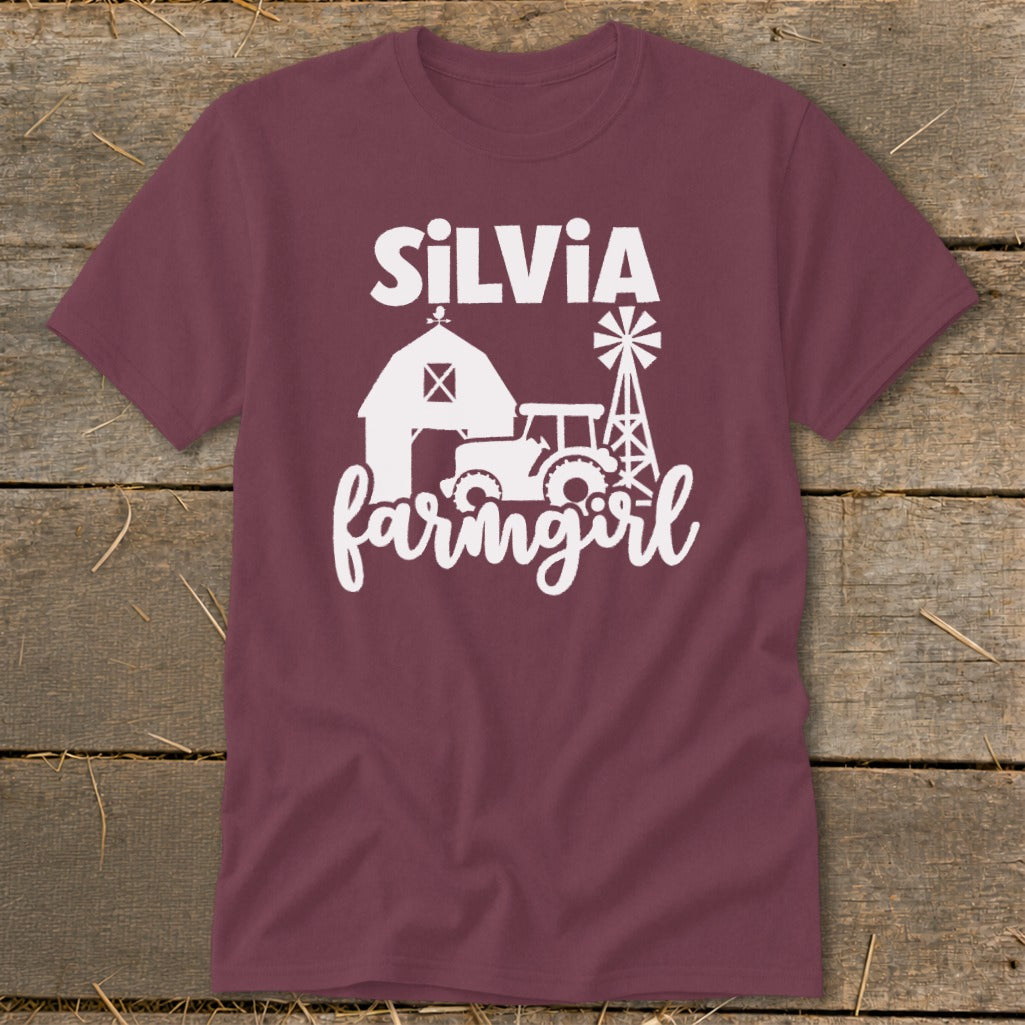 Maroon t-shirt with white text "SiLVIA farmgirl" and barn, tractor, windmill graphic.