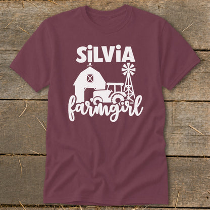 Maroon t-shirt with white text "SiLVIA farmgirl" and barn, tractor, windmill graphic.