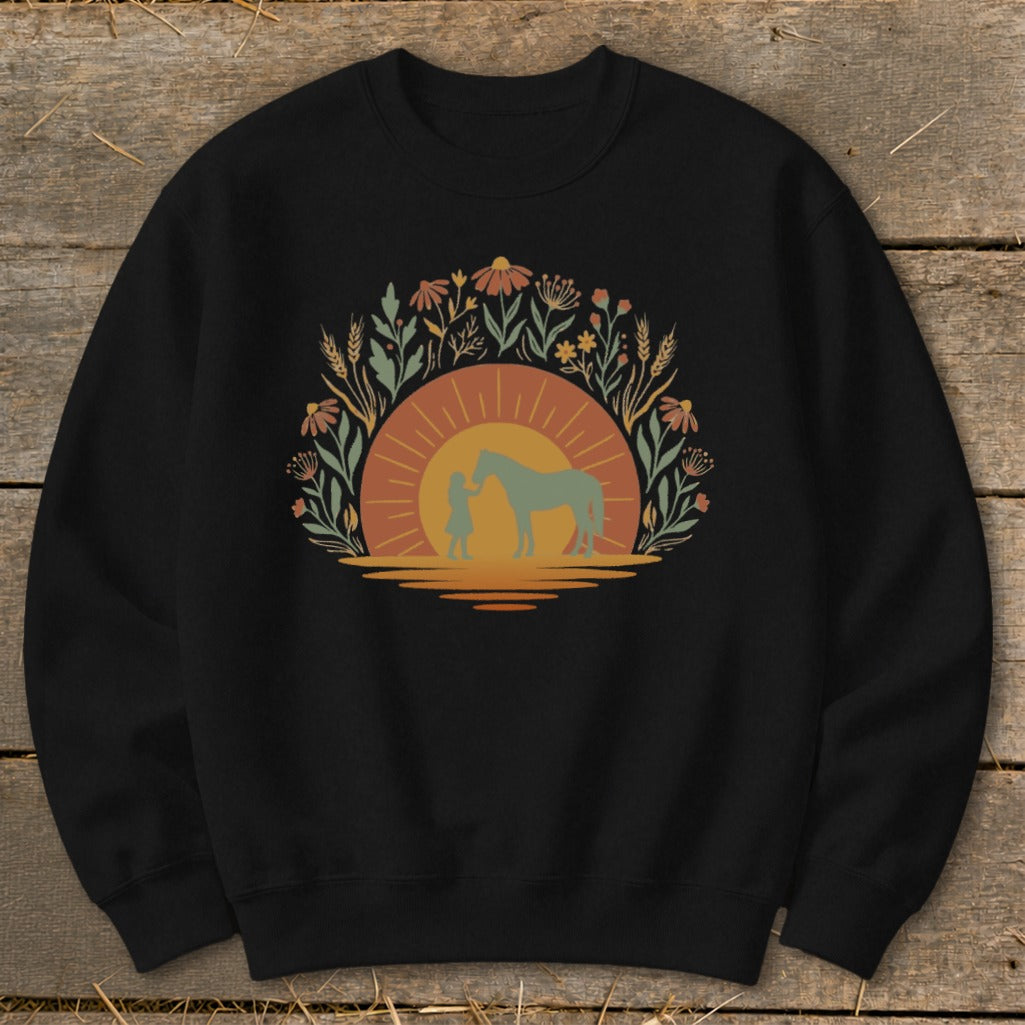 Black sweatshirt with a sunset graphic of a child and horse within floral and wheat wreath.