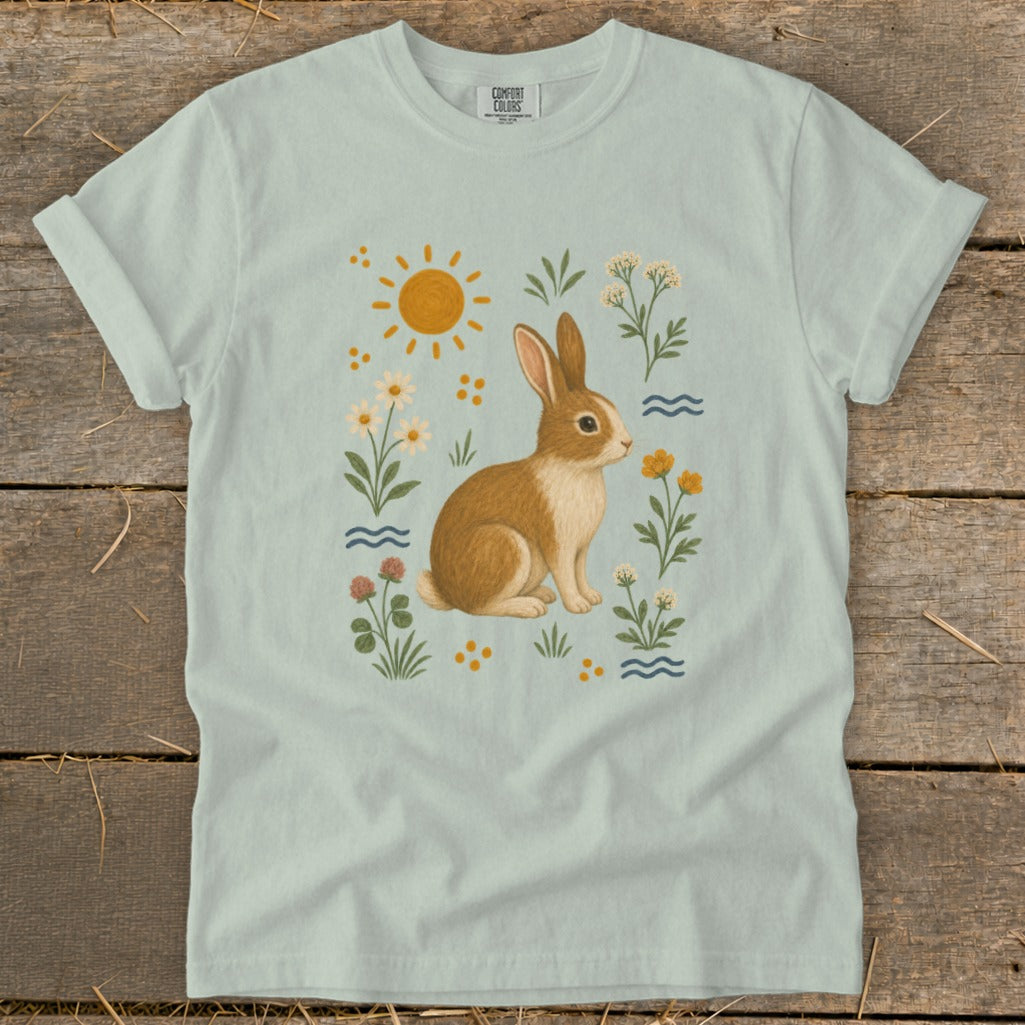Light blue t-shirt with a brown bunny surrounded by flowers, sun, and waves graphic.