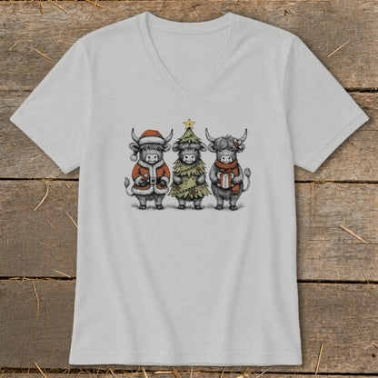 Three Highland cows in festive Christmas attire stand in a line on a grey t-shirt.