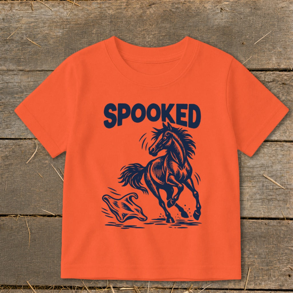 Orange t-shirt with navy text "SPOOKED" above a startled horse facing a ghost.