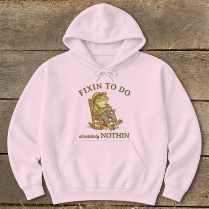 Pink hoodie with cartoon frog in rocking chair, text "FIXIN TO DO absolutely NOTHIN".