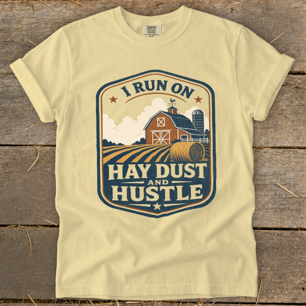 Pale yellow t-shirt with a farm scene and text "I RUN ON HAY DUST AND HUSTLE".
