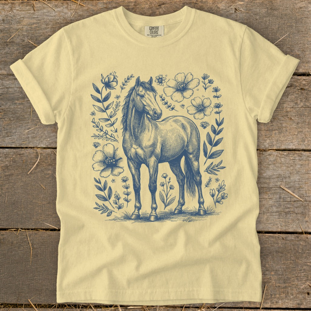 Pale yellow t-shirt with blue sketch of a horse surrounded by flowers.