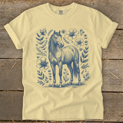 Pale yellow t-shirt with blue sketch of a horse surrounded by flowers.
