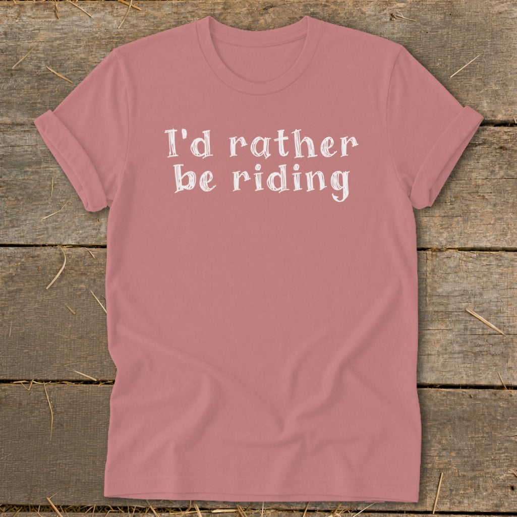 Rose t-shirt with white text "I'd rather be riding" on a wooden background.