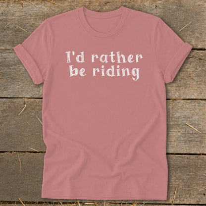 Rose t-shirt with white text "I'd rather be riding" on a wooden background.