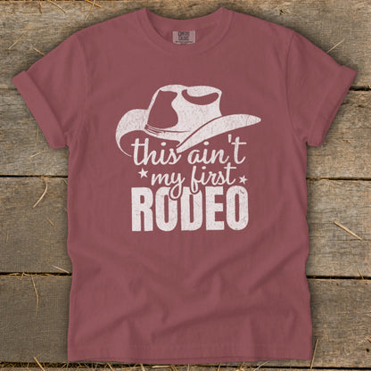 Dusty rose t-shirt with white cowboy hat graphic and "this ain't my first rodeo" text.