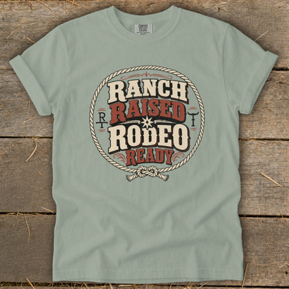 Sage green t-shirt featuring a circular graphic with a rope border and the text Ranch Raised Rodeo Ready.