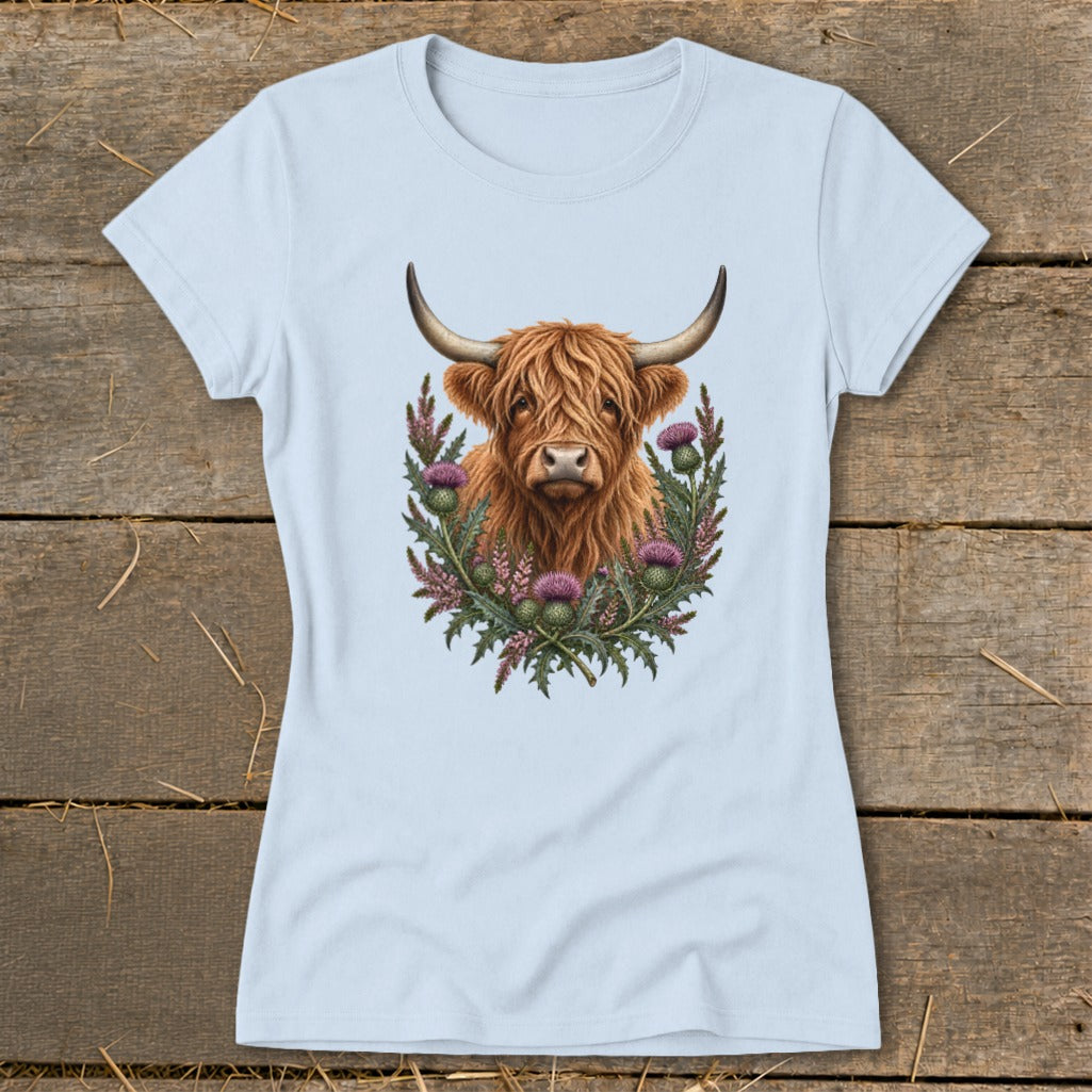 Highland cow portrait surrounded by thistles and greenery on a light blue t-shirt.