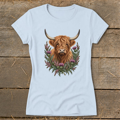 Highland cow portrait surrounded by thistles and greenery on a light blue t-shirt.
