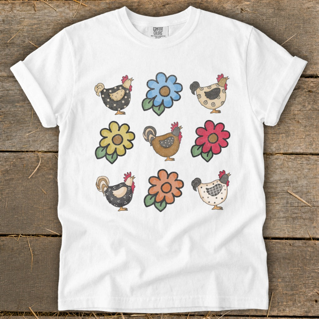 White t-shirt with a print of nine whimsical chickens and flowers.