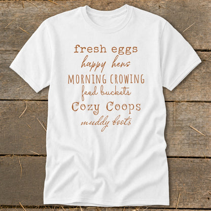 White t-shirt with brown text: "fresh eggs happy hens MORNING CROWING feed buckets Cozy Coops muddy boots"