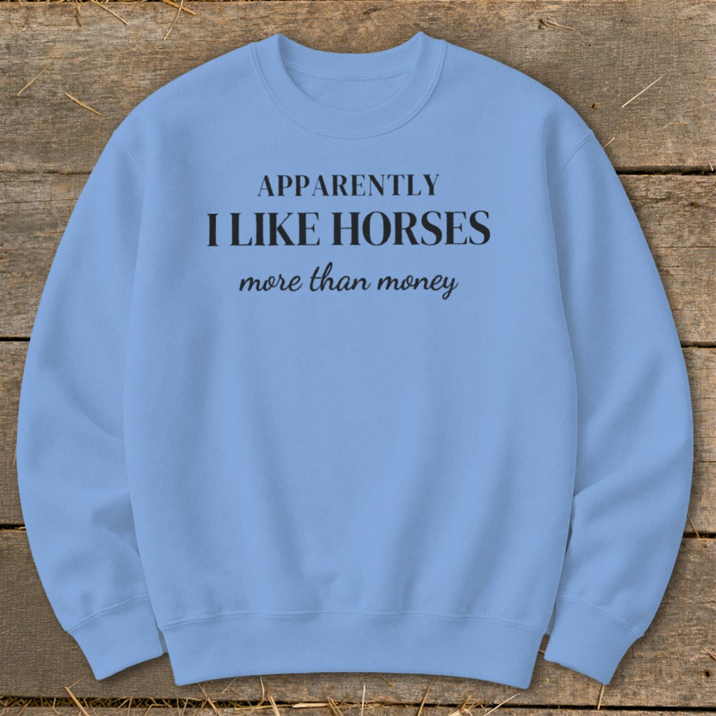 Light blue crewneck sweatshirt with black text reading "APPARENTLY I LIKE HORSES more than money".
