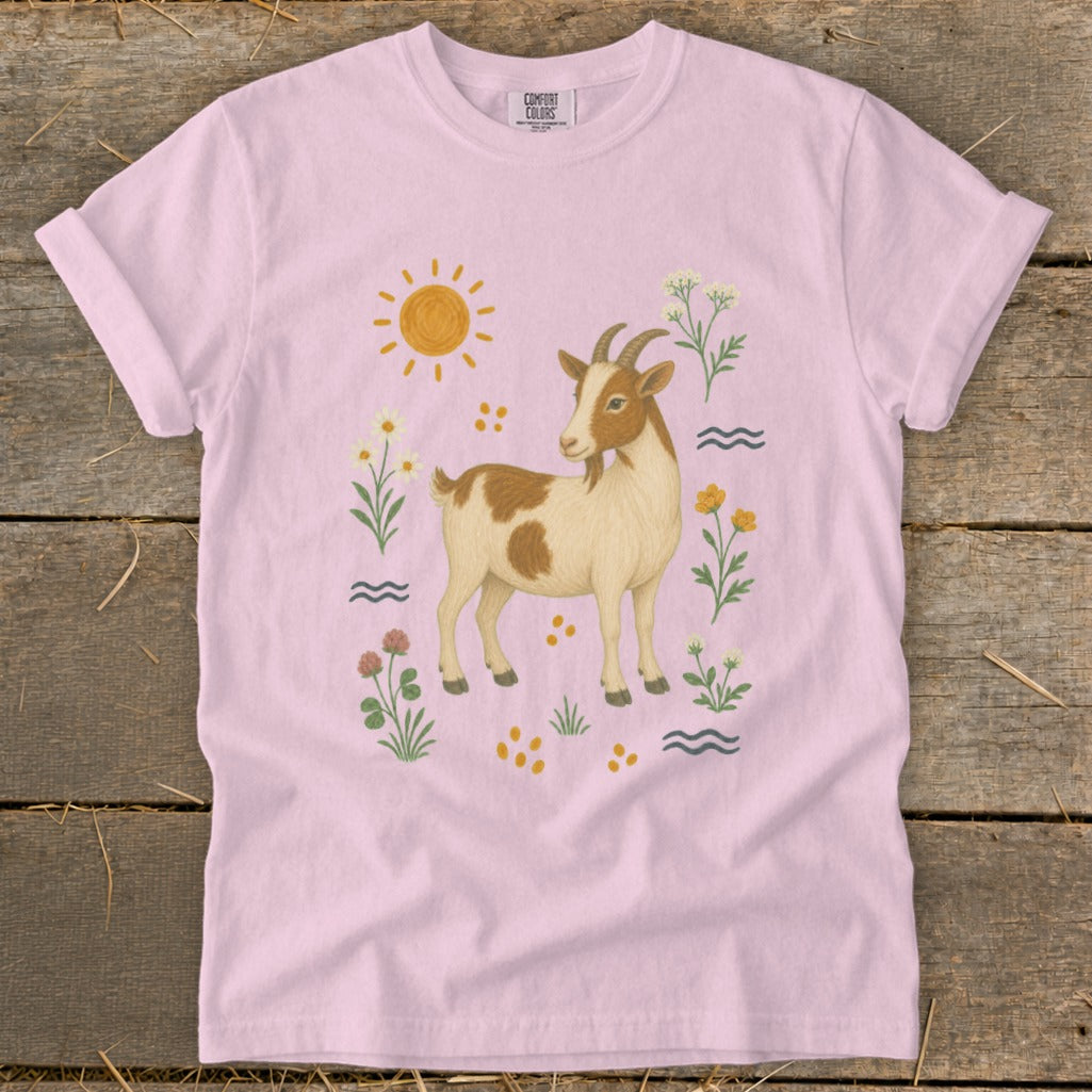 Pink t-shirt with a brown and white goat, sun, flowers, and wavy lines.