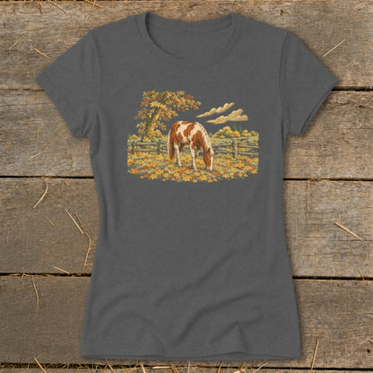 Brown and white horse grazing in a field of autumn leaves with a wooden fence.