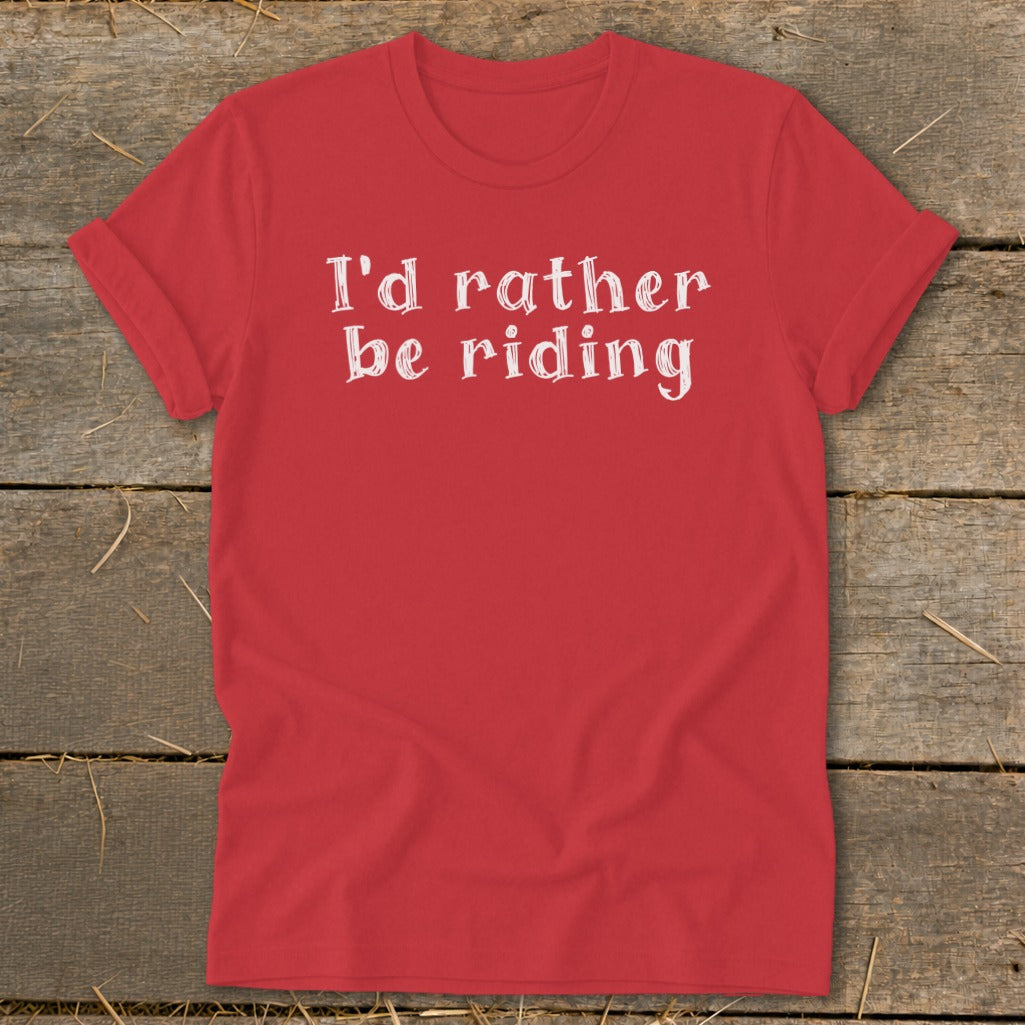Red t-shirt with white text "I'd rather be riding" on a wooden background.