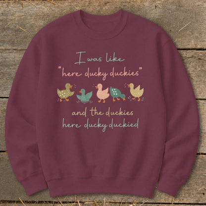 Burgundy sweatshirt with cartoon ducks and text "I was like 'here ducky duckies' and the duckies here ducky duckied".