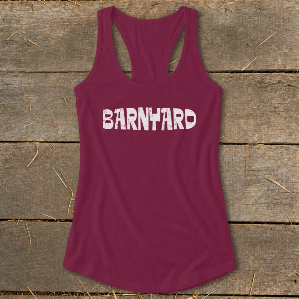 Maroon women's racerback tank top with distressed white text reading BARNYARD laid on a rustic wooden background.